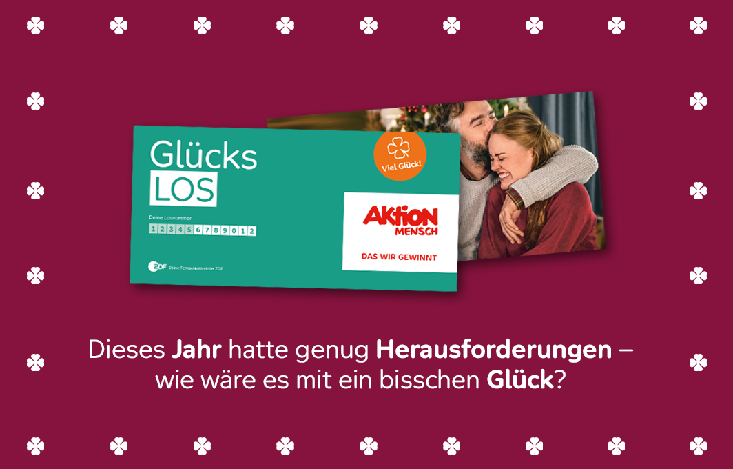 Ein Glücks-Los auf rotem Hintergrund. Daneben ein Mann und eine Frau, die sich lachend im Arm halten. Darunter steht: Dieses Jahr hatte genug Herausforderungen – wie wäre es mit ein bisschen Glück? Das Bild ist umrahmt von vierblättrigen Kleeblätter