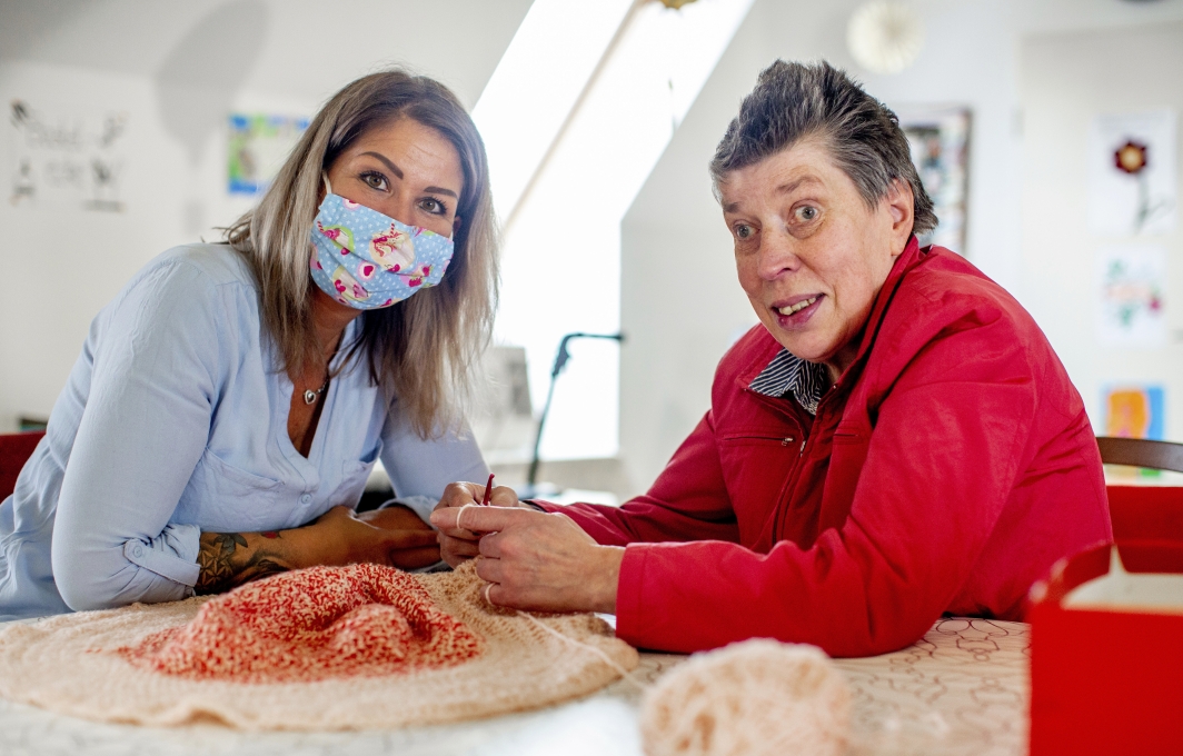 Zwei Frauen mit und ohne Behinderung sitzen gemeinsam an einer Handarbeitsarbeit.