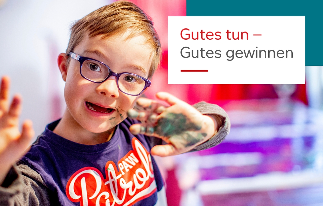Ein Junge mit Downsyndrom hält lachend seine farbverschmierten Hände in die Kamera.