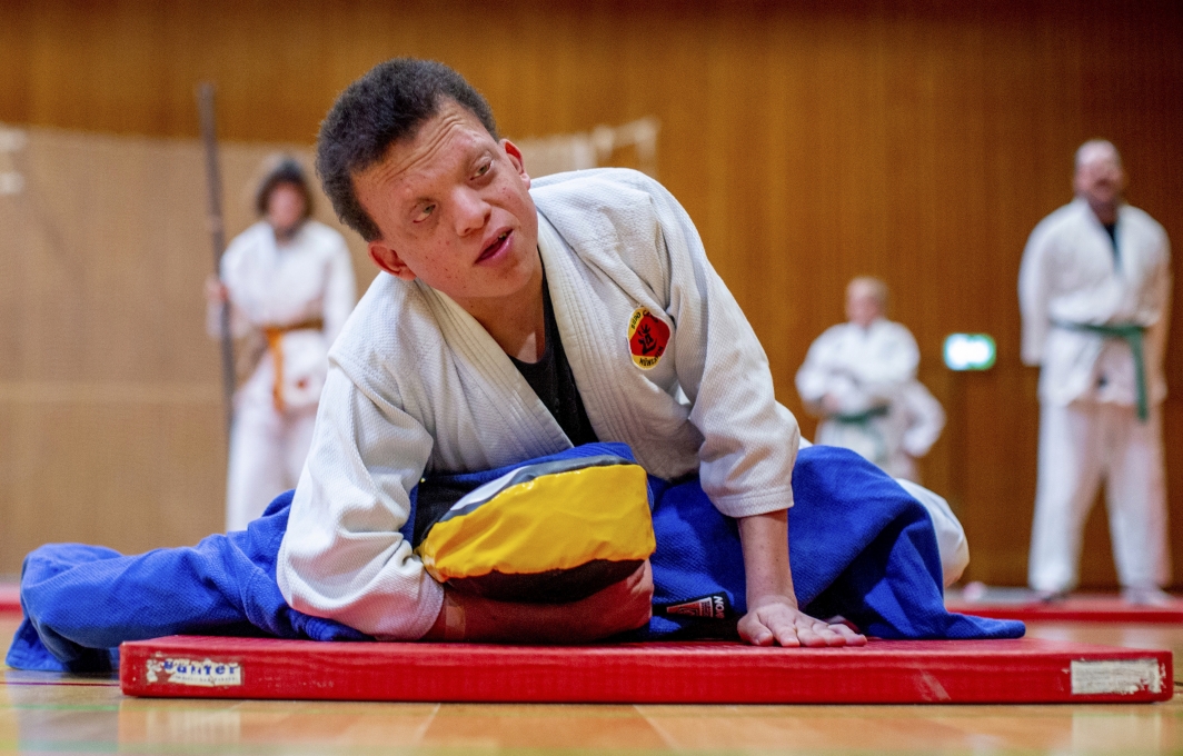 Junger Mann mit Behinderung im Judo-Anzug liegend auf Judo-Matte.