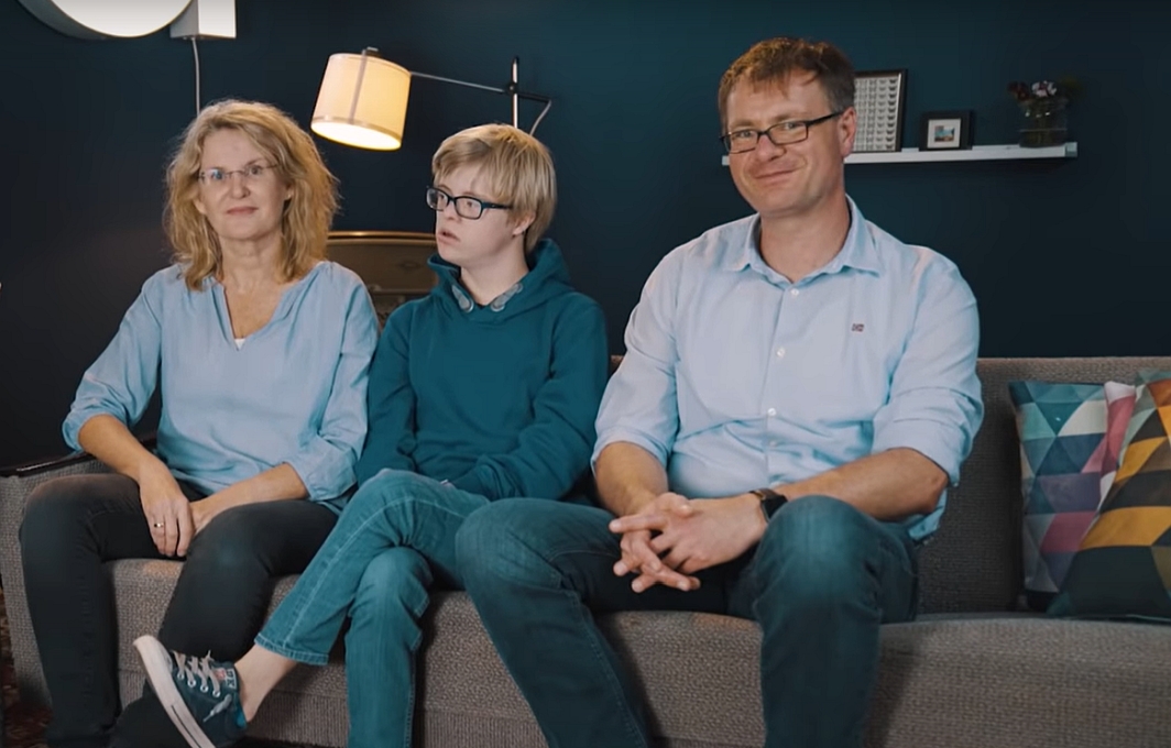 Eine Frau und ein Mann sitzen gemeinsam mit ihrem 17-jährigen Sohn auf einem Sofa.