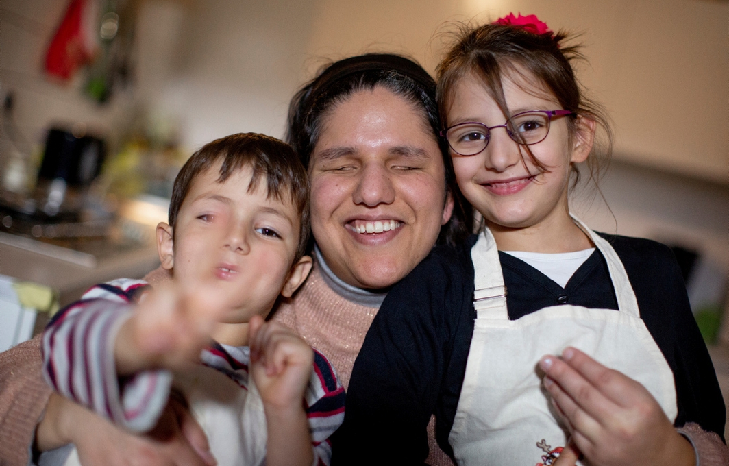 Eine Mutter mit Sehbehinderung hält ihre zwei Kinder im Arm. Alle lachen fröhlich in die Kamera.