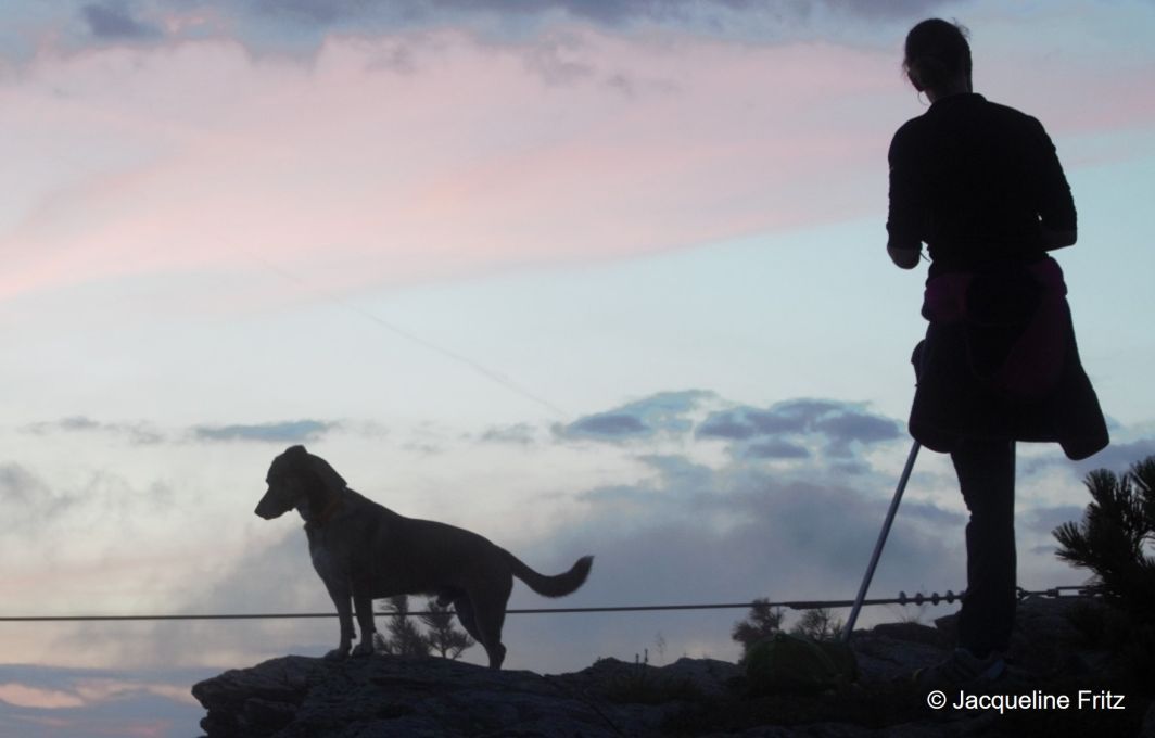Die Silhouette einer einbeinigen Frau im Abendrot auf dem Gipfel eines Berges.