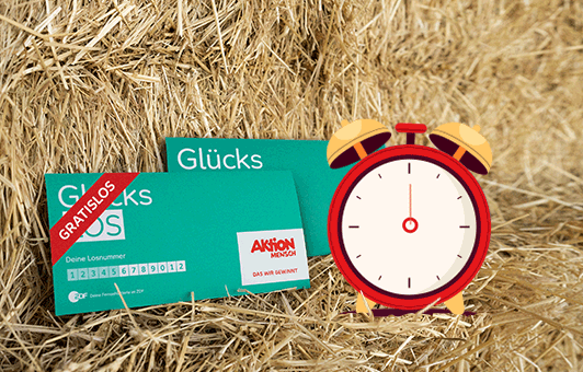 Zwei Glücks-Lose liegen im Heu und ein Wecker springt in die Luft.