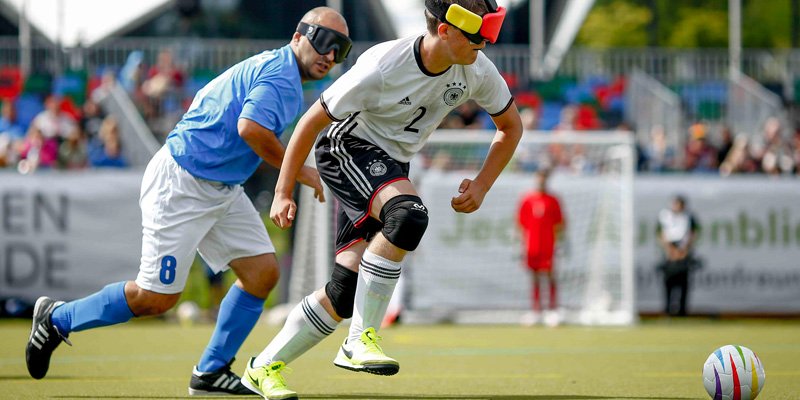 Zwei blinde Männer jagen dem Fußball hinterher.