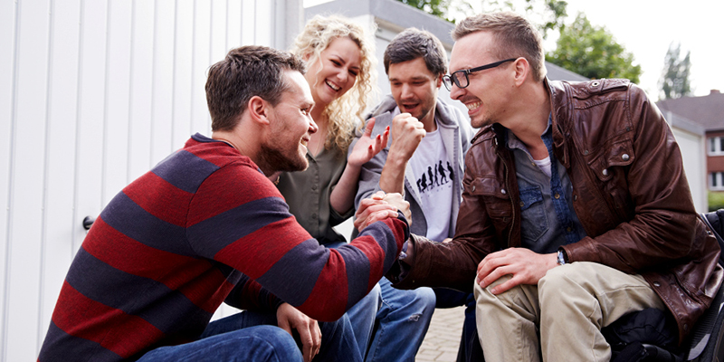 Eine Gruppe junger Menschen mit und ohne Behinderung sitzen in einem Innenhof beisammen und schlagen sich jubelnd in die Hände ab.