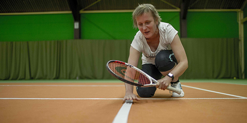 Blinde Frau ertastet die Markierungslinie eines Tennisfeldes