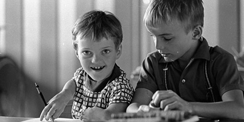 Ein Schwarz-Weiß-Foto: Zwei Jungen mit und ohne Behinderung sitzen an einem Schreibtisch.