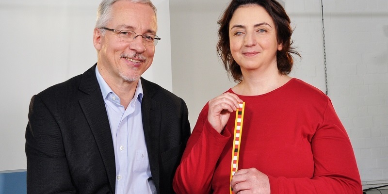 Frank und Filiz sitzen nebeneinander mit Hilfsmitteln zur Tastuntersuchung in der Brustkrebsvorsorge