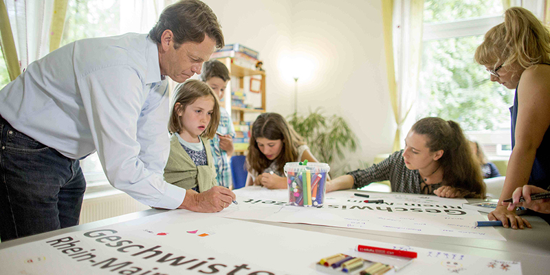 Rudi Cerne gestaltet zusammen mit Kindern ein Plakat