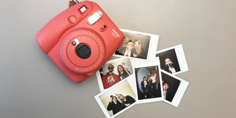 Eine rote Instax-Kamera liegt mit Polaroids auf einem Tisch.
