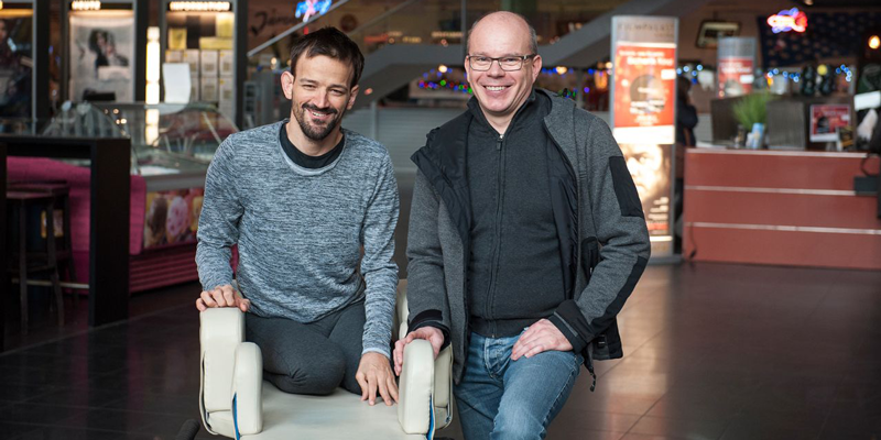 Zwei Männer am Eingang des Kinos, einer von ihnen sitzt im Rollstuhl.