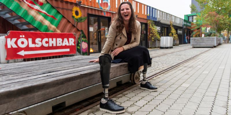 Eine junge Frau sitzt lachend auf einer Bank. Neben ihr steht ihre Beinprothese.