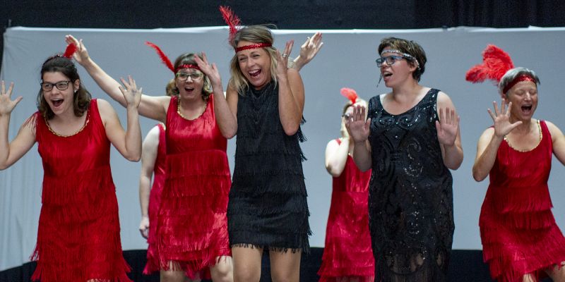 Mehrere Frauen in rotem oder schwarzem Kleid auf einer Theaterbühne.