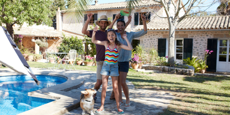 Eine Familie mit Hund steht an einem Pool und jubelt.