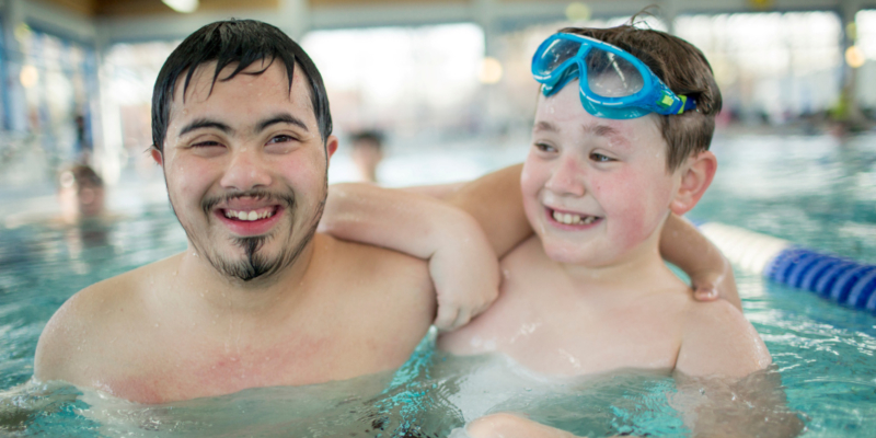 Zwei Jungen mit und ohne Behinderung im Schwimmbad, sie lächeln in die Kamera.