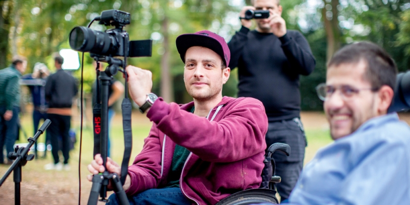 Ein junger Mann im Rollstuhl bringt eine Videokamera in Position.