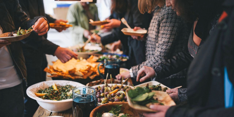 Mehrere Personen stehen an einem Buffet-Tisch und haben Teller in den Händen.