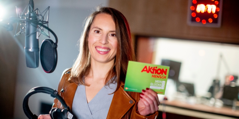 Sängerin Svenja Weierich steht im Tonstudio und hält lächelnd ihr Glücks-Los in die Kamera.