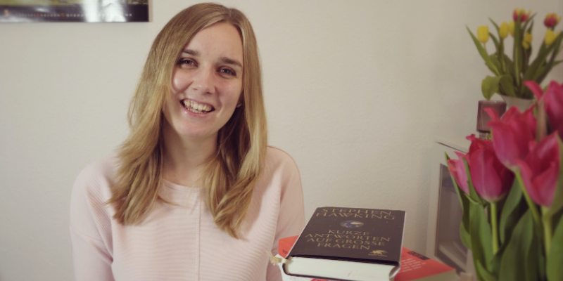 Die Vloggerin Fabie sitzt in ihrem Zimmer, vor sich hat sie einen Strauß Tulpen und einen Stapel Bücher.