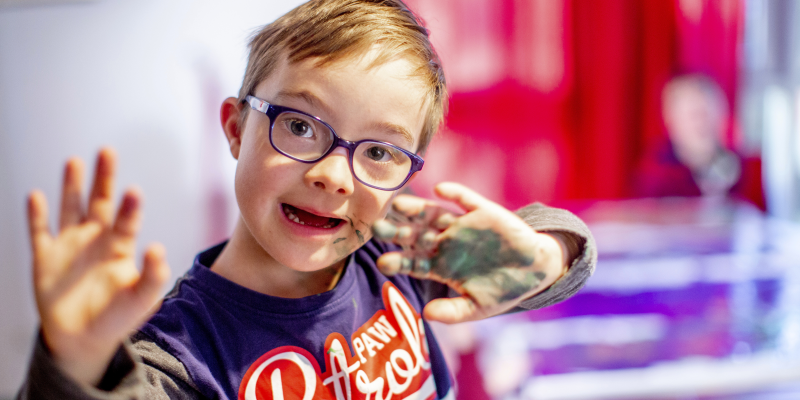 Ein Kind mit Down Syndrom hält seine bunten Hände in die Kamera
