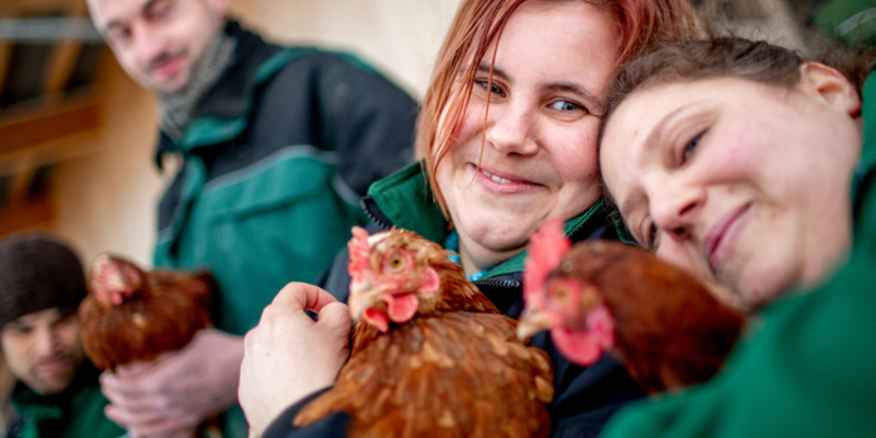Zwei Frauen halten jeweils ein Huhn in den Armen und lächeln in die Kamera.