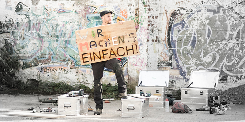 Mann hält ein Brett in der Hand. Zu lesen ist: "Wir machens einfach"