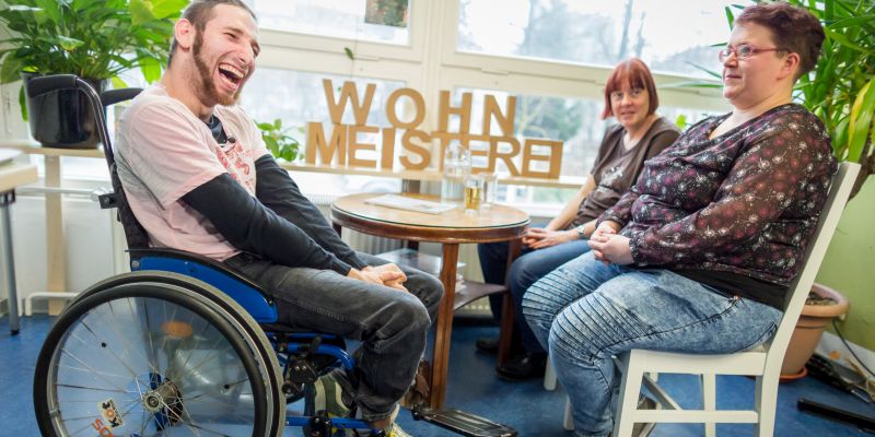 Ein Mann im Rollstuhl und eine Frau sitzen an einem Beratungstisch.