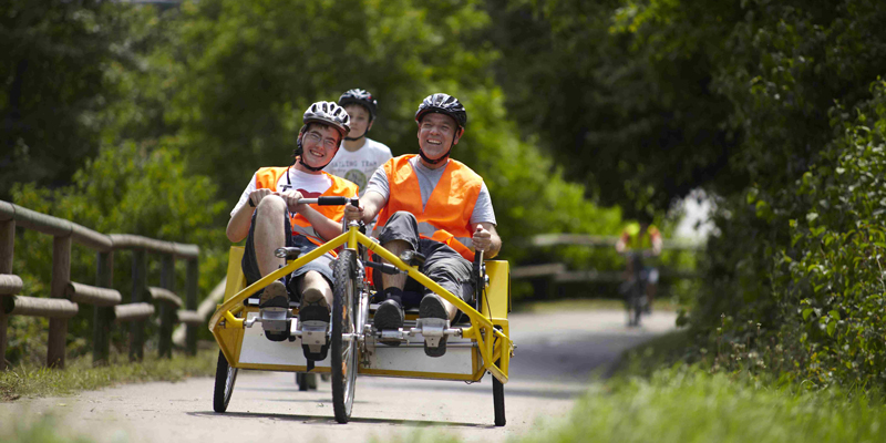 Zwei Männer fahren mit einem Rollstuhlfahrrad