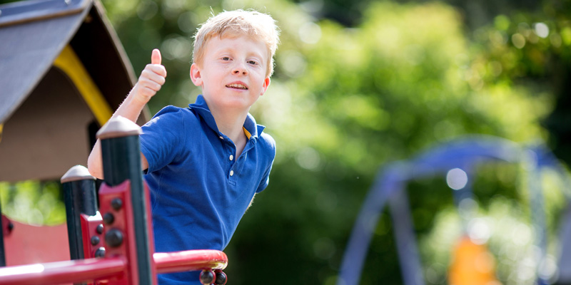 Ein Junge auf einem Spielplatz zeigt den Daumen hoch