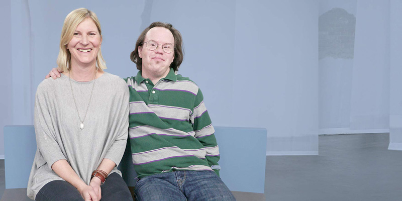 Eine Frau und ein Mann mit Down-Syndrom sitzen auf einer Bank.