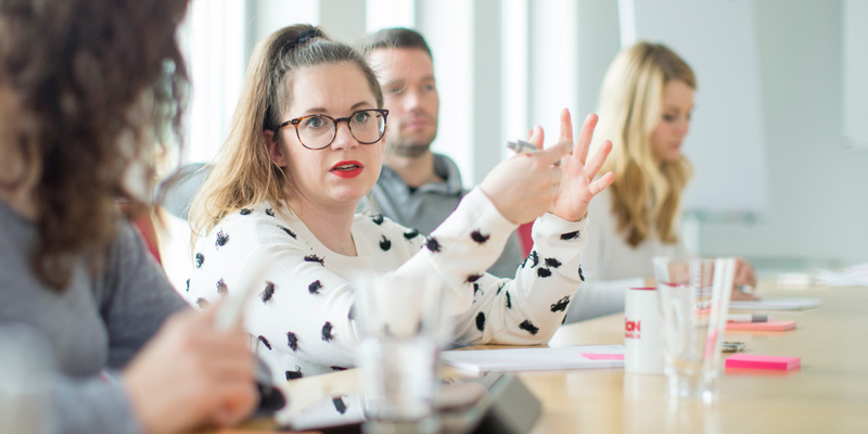 Eine Frau sitzt an einem Konferenztisch und spricht.