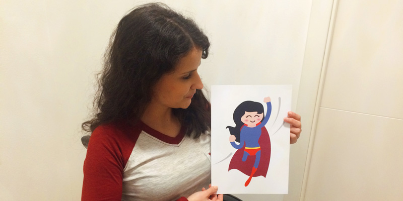 Eine Frau im Rollstuhl hält ein Blatt Papier mit einem Superhelden-Emoji mit einem Bein in der Hand.
