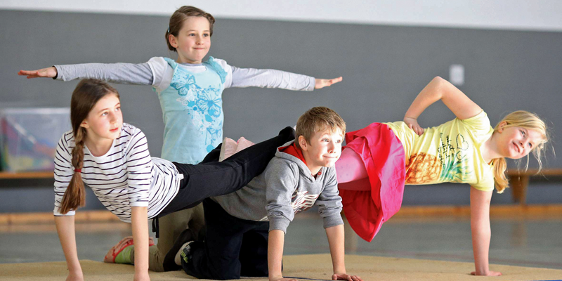 Verschiedene Kinder machen eine Pyramide in einer Sporthalle.