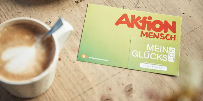 Ein Glücks-Los liegt auf einem Tisch. Daneben steht eine Tasse Kaffee.