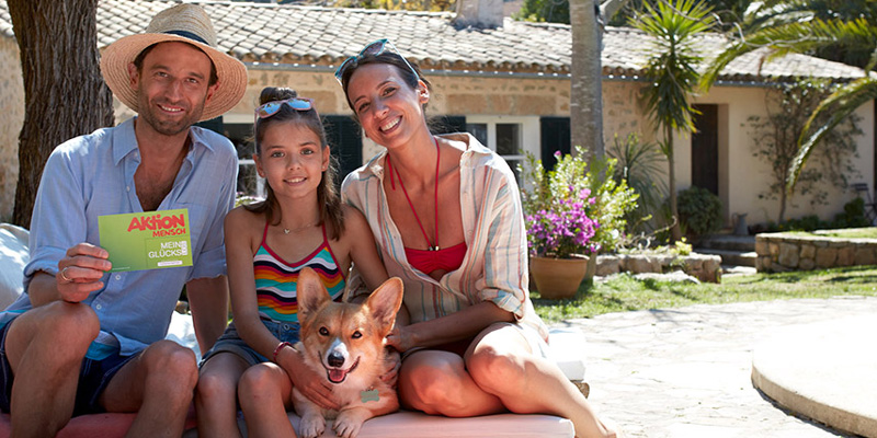 Eine Familie sitzt am Pool, der Mann hält ein Glücks-Los in der Hand.