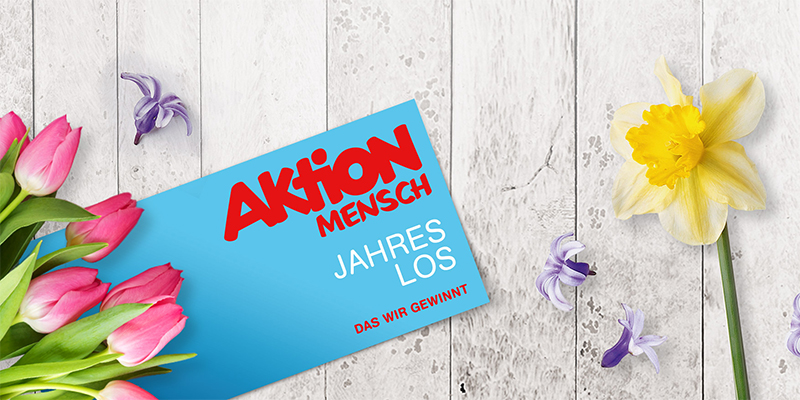 Ein Jahreslos liegt neben Blumen auf einem Holztisch
