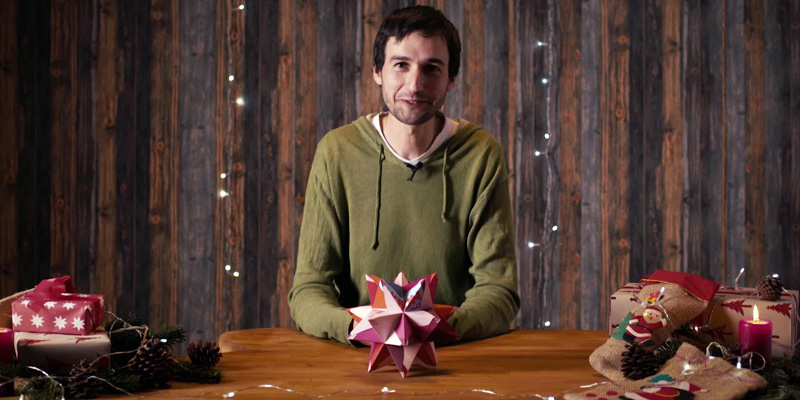 Ein Mann sitzt an einem Tisch. Vor ihm liegt ein Origami-Stern.