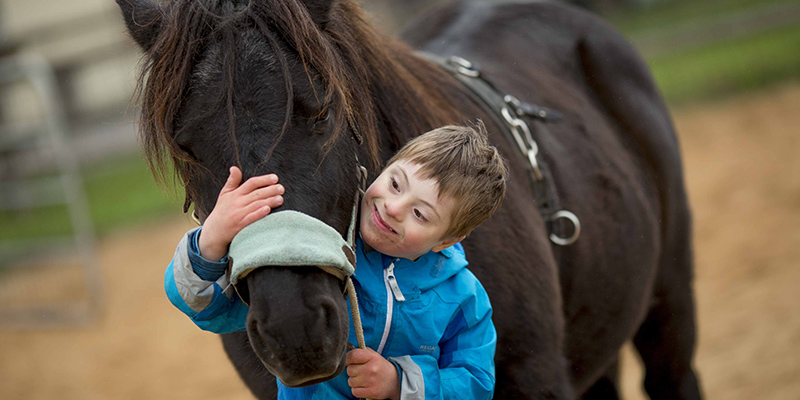 Ein Junge mit Down-Syndrom umarmt ein Therapie-Pferd