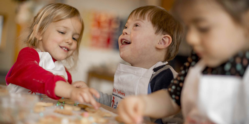 Zwei Kinder mit und ohne Behinderung backen gemeinsam Weihnachtsplätzchen.