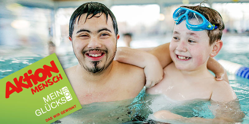 Zwei Jugendliche mit Behinderung im Schwimmbad, davor ein Glücks-Los.
