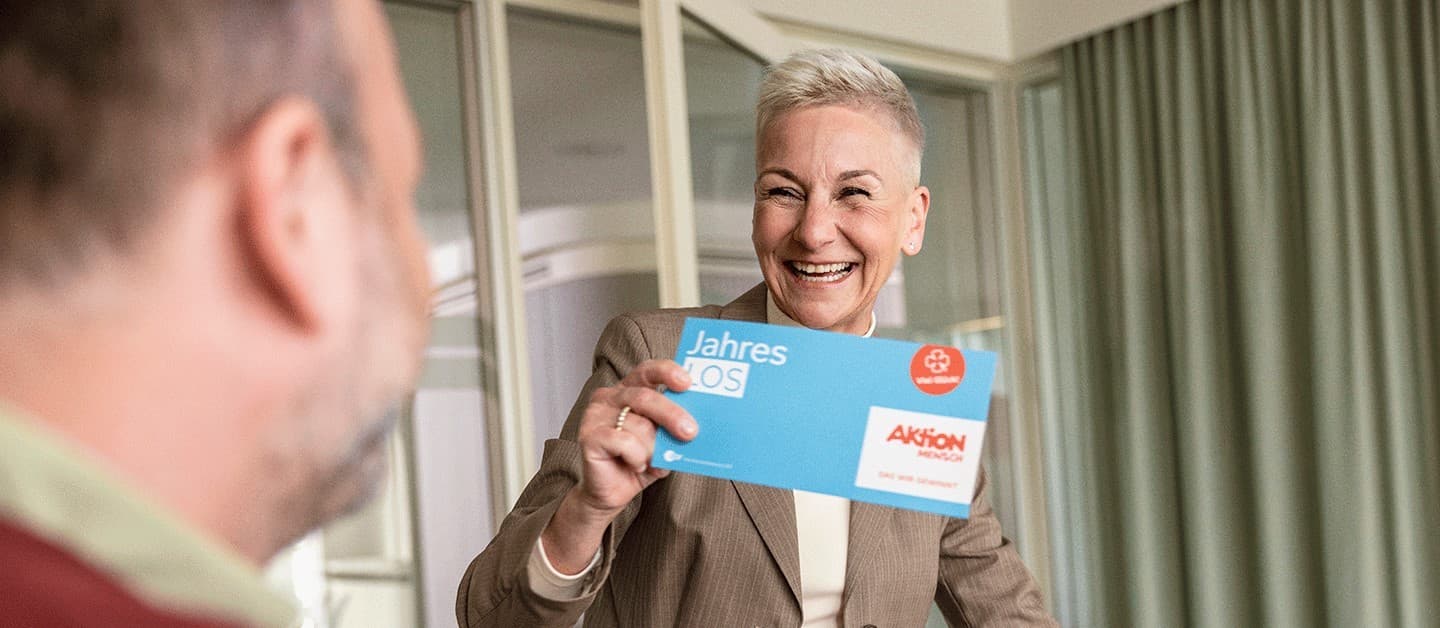 Mitarbeiterin freut sich über Aktion Mensch Jahreslos, das sie als Geschenk von ihrem Arbeitgeber erhalten hat.
