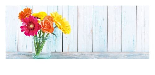 Bunte Blumen im Glas vor einer Holzbohlenwand