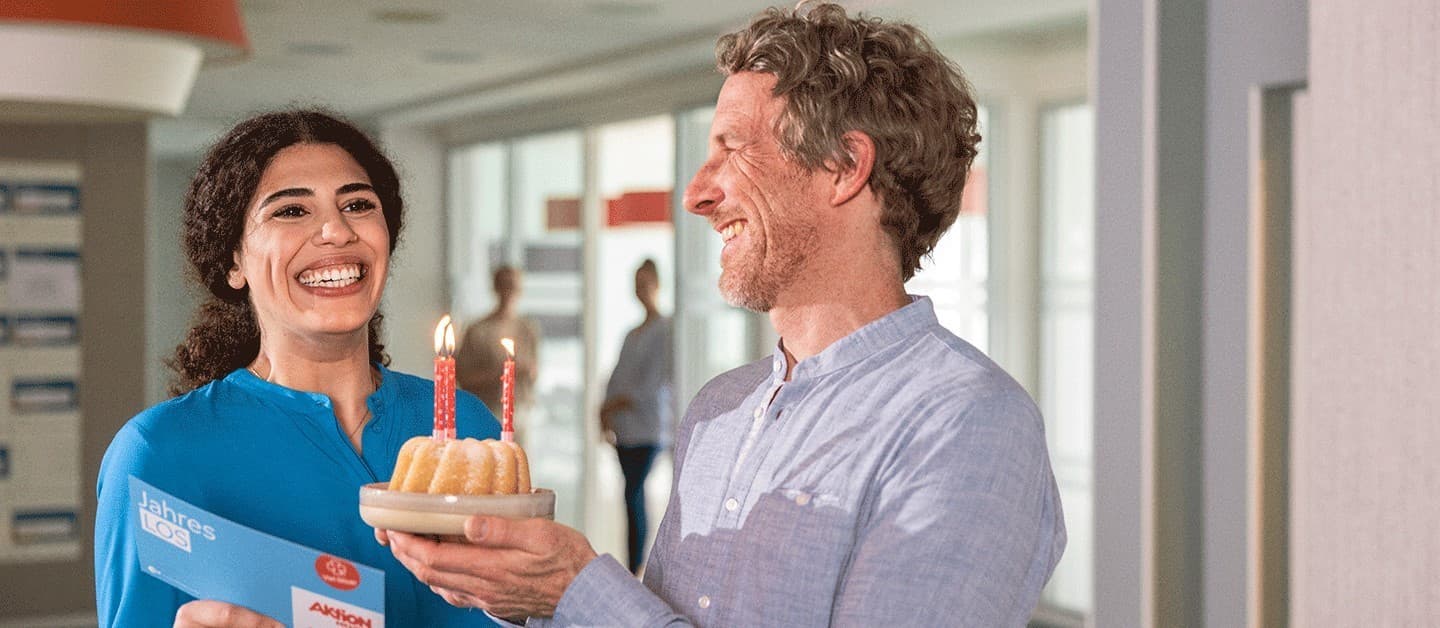 Frau erhält Aktion Mensch Jahreslos zum Geburtstag und bekommt einen Kuchen überreicht.