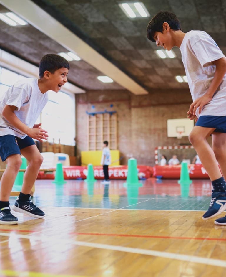 Zwei Jungen spielen Basketball in einer Sporthalle.