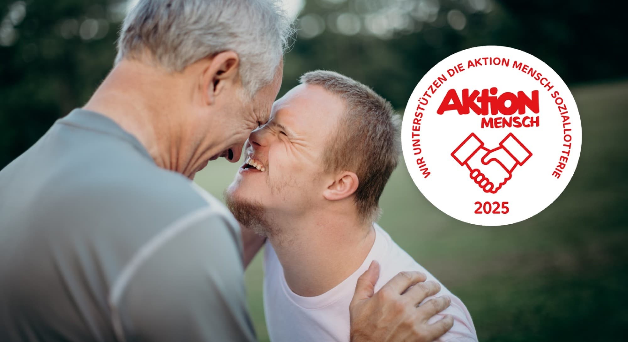 Zwei Männer blicken sich Stirn an Stirn freudig lächelnd an.